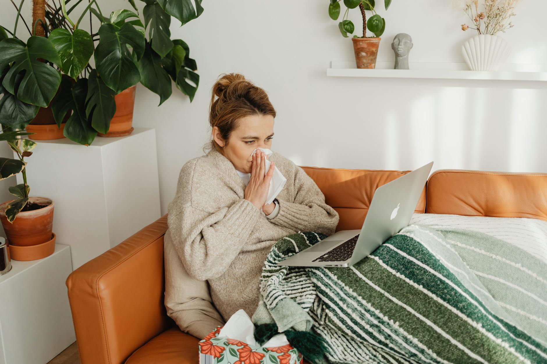 woman wiping her nose while using a laptop on sofa